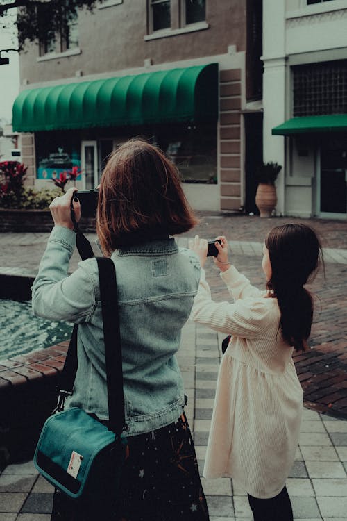 Mother and Daughter Standing Beside Each Other while Taking Photos Using a Cellphone