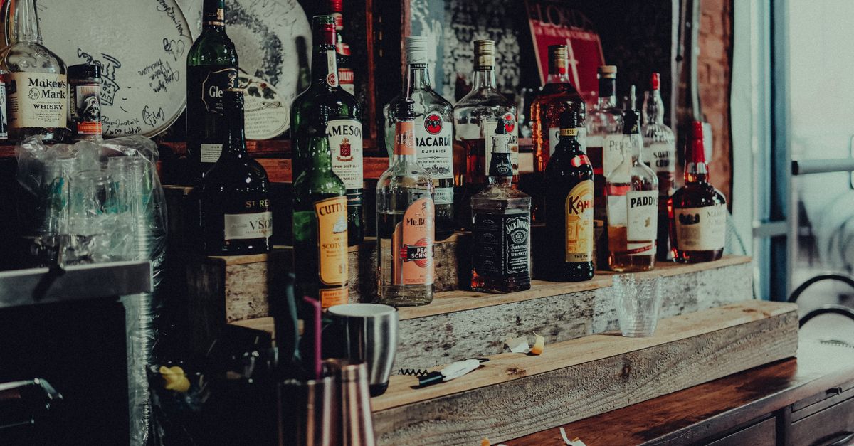A collection of diverse liquor bottles including whisky, rum, and vodka displayed on a wooden bar shelf.