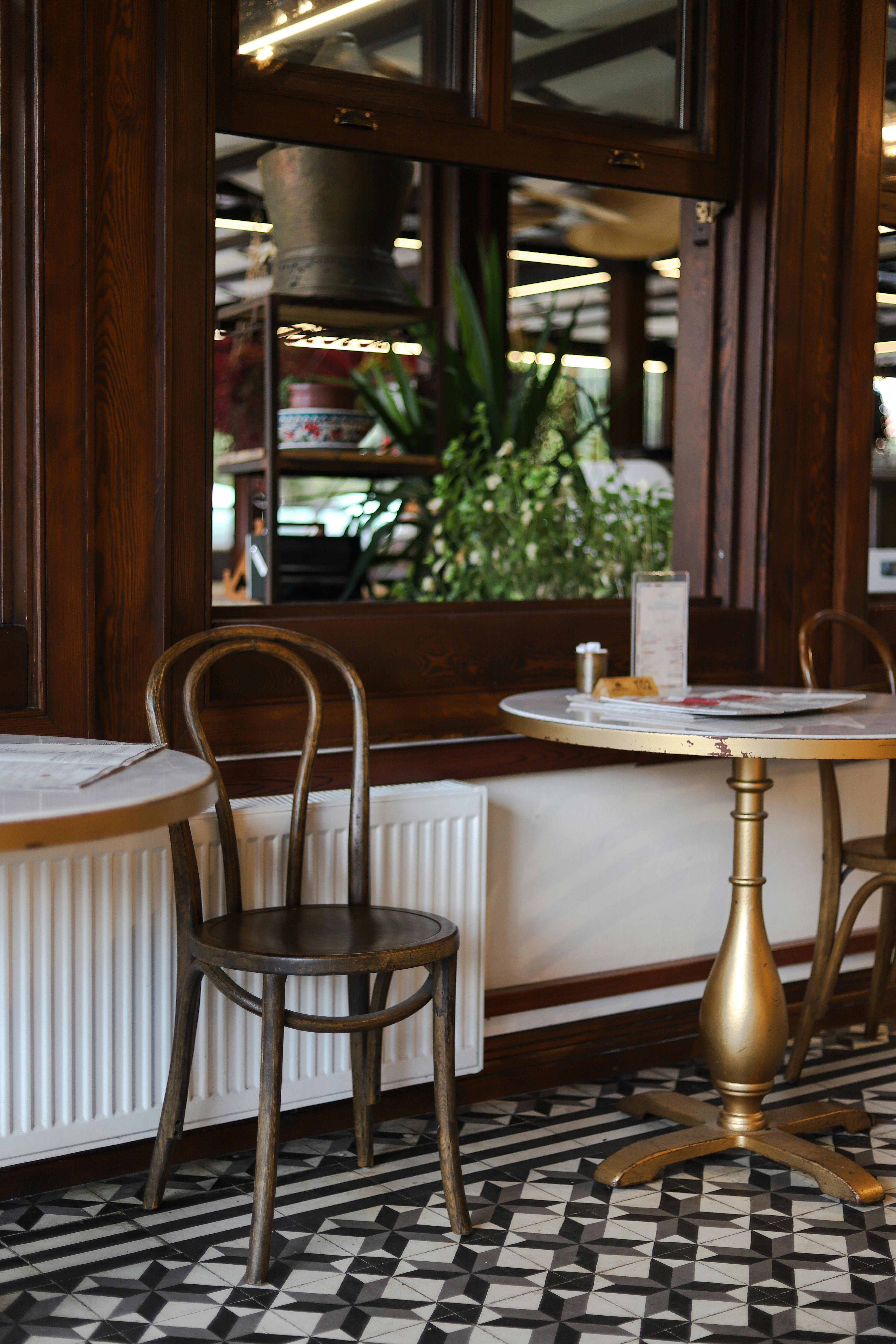 Elegant indoor café setting featuring a vintage wooden chair, marble table, and lush greenery.