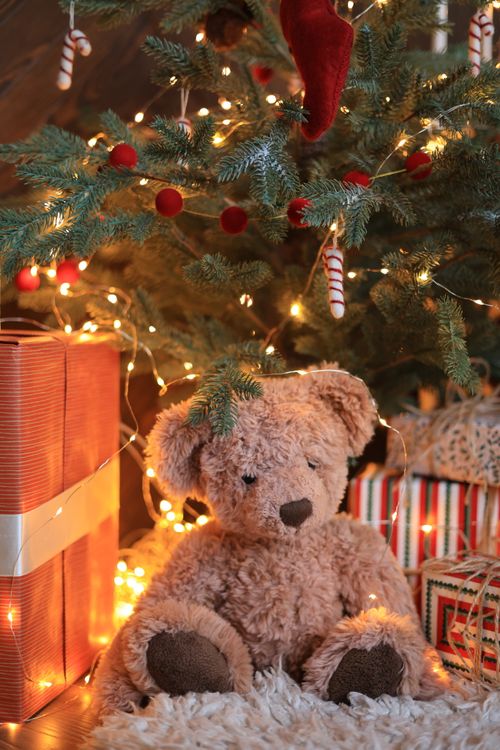 Free A warm Christmas setting featuring a teddy bear under a decorated tree with presents. Stock Photo