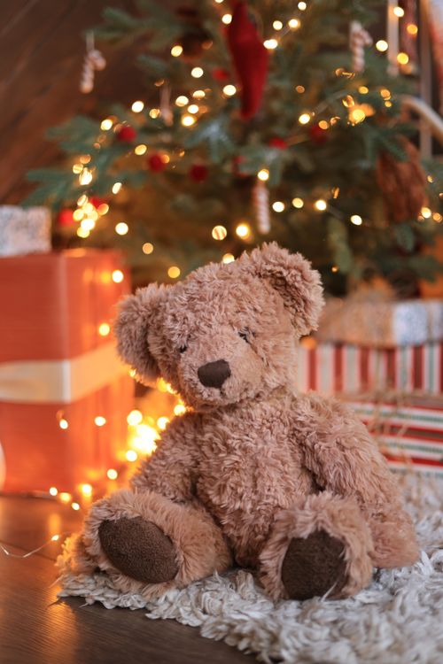 Free Soft teddy bear under a warm Christmas tree with festive lights and gifts. Stock Photo