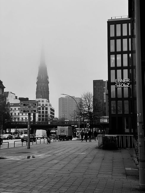Black and white photo of a foggy day in downtown Hamburg with St. Nikolai tower visible.