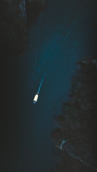 A solitary boat travels through dark, tranquil waters with surrounding nature.