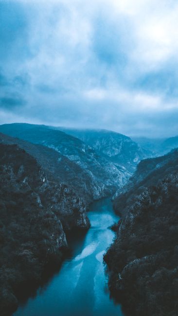 A breathtaking aerial view of a river gorge surrounded by lush mountains under a cloudy sky.