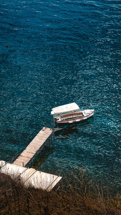 Free A serene view of a wooden boat docked at a quiet pier on a glistening blue water surface. Stock Photo