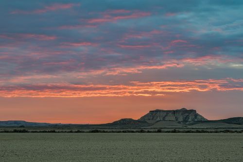 Free A stunning sunset illuminating a barren landscape with dramatic clouds and distant mountains. Stock Photo