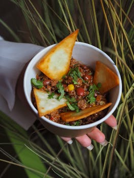 Bowl of chili con carne topped with crispy tortilla chips and fresh coriander.