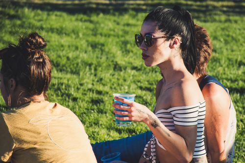 Free Woman with sunglasses and tattoo enjoying leisure time outdoors holding a drink. Stock Photo