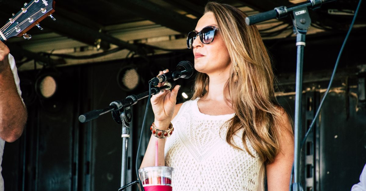 A woman in sunglasses sings on stage during an outdoor concert, exuding confidence and style.