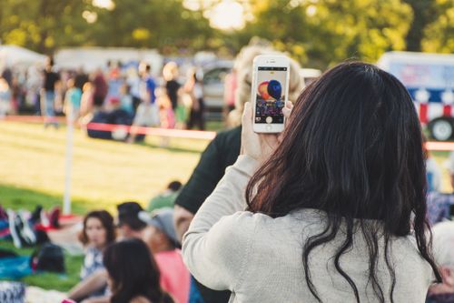 Free A woman captures a lively outdoor festival scene with her smartphone. Stock Photo