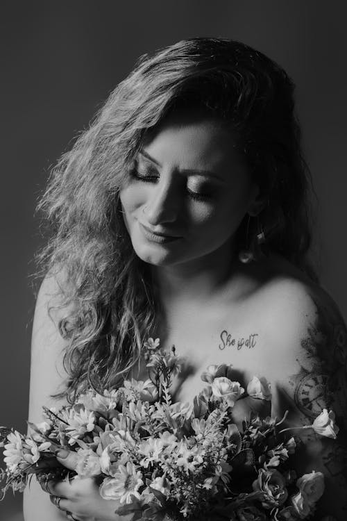 A Grayscale Photo of a Tattooed Woman Holding Flowers