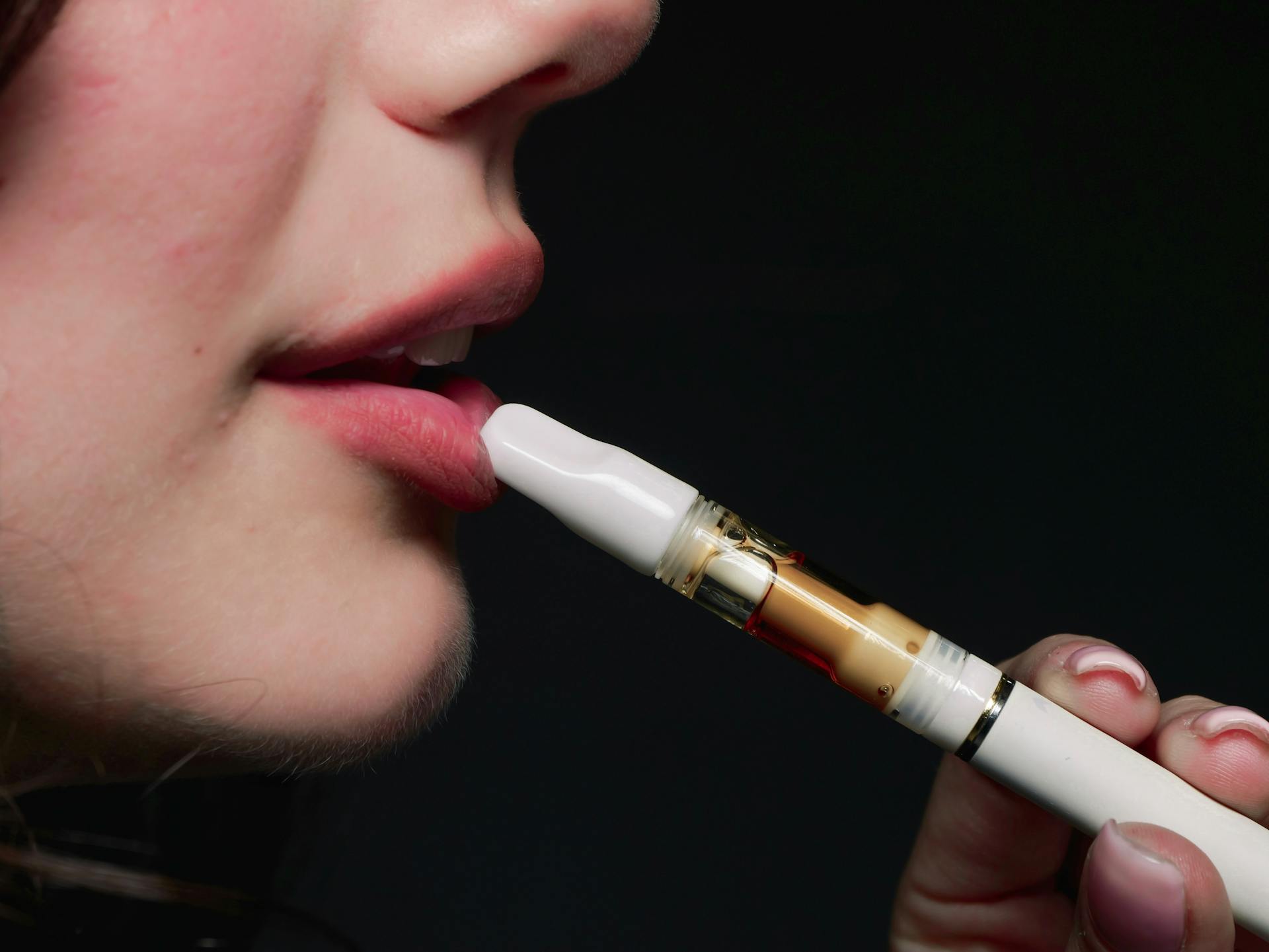 Close-up image of a woman vaping with an e-cigarette on a dark background.