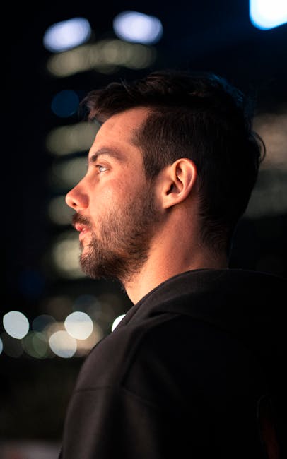 Portrait of a young man in a hoodie, gazing thoughtfully in a cityscape at night.