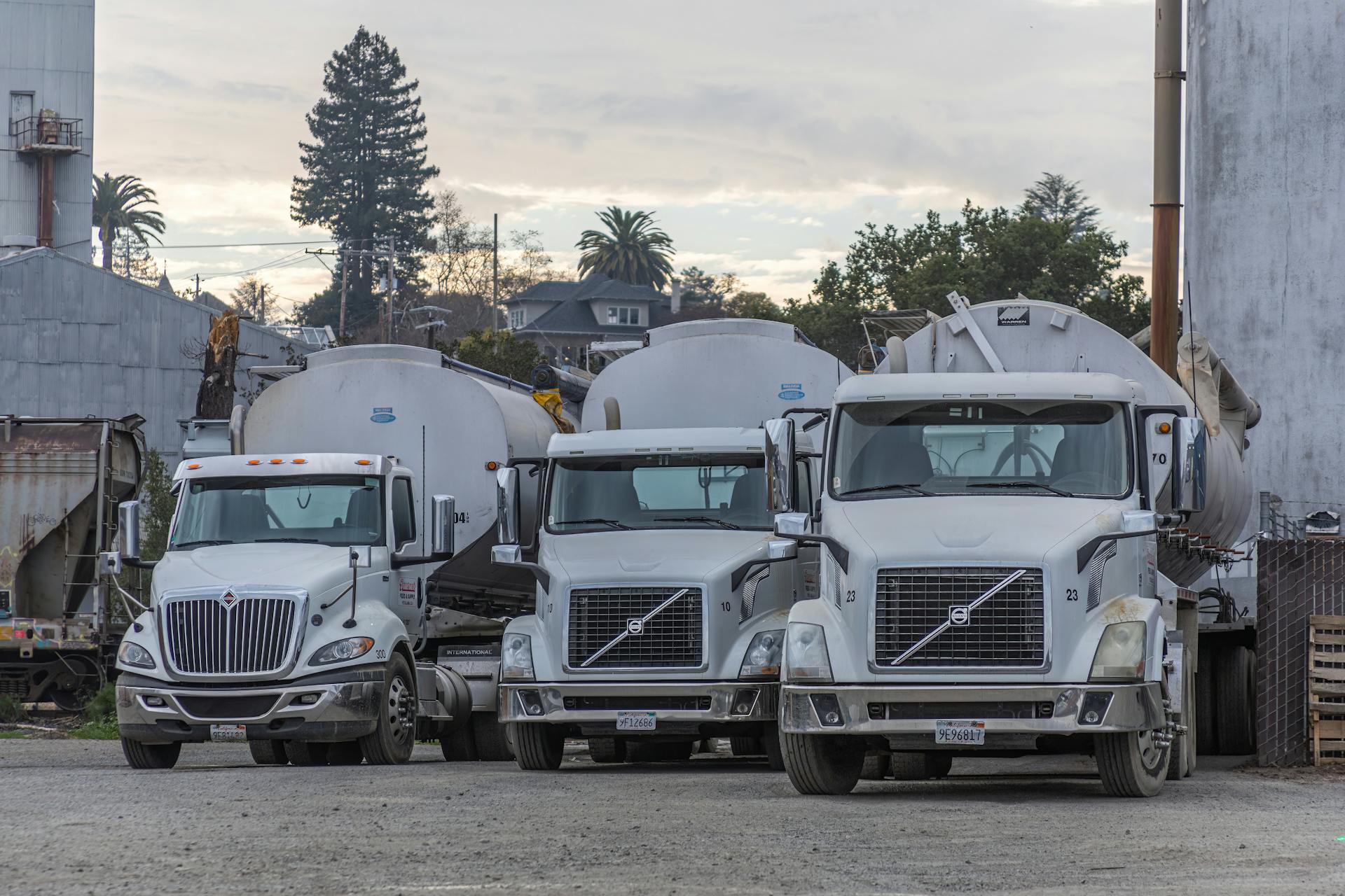 A row of white trucks parked in an industrial factory setting. Ideal for transport and logistics themes.