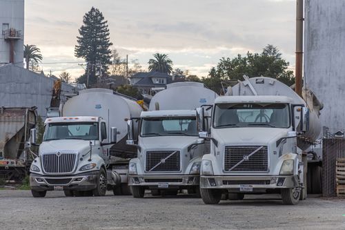Free A row of white trucks parked in an industrial factory setting. Ideal for transport and logistics themes. Stock Photo