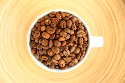 Free A close-up of roasted coffee beans in a white mug on a wooden surface, shot from above. Stock Photo