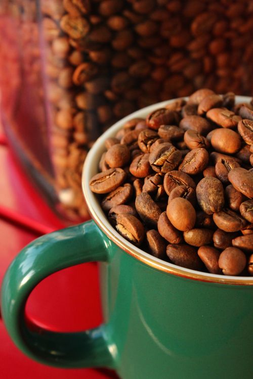 Free Close-up of coffee beans spilling over a green cup with a red background. Perfect for cafés and coffee shops. Stock Photo