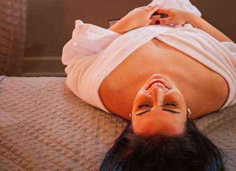 Smiling woman lying upside down in a bathrobe, enjoying a moment of relaxation indoors.