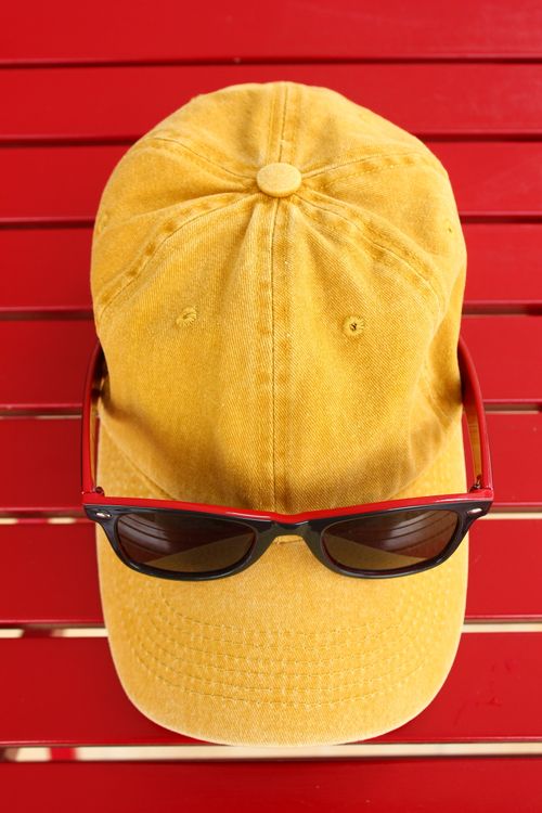 Free Yellow baseball cap with sunglasses laid on a vibrant red background, creating a bold fashion statement. Stock Photo