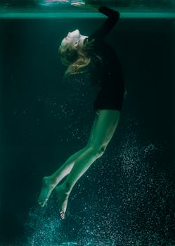 在昏暗的绿松石色灯光下，一名女子以宁静的姿势漂浮，被捕捉成一张优雅的水下照片