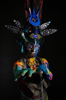 Colorful fantasy performer posing with intricate body paint and costume in a dramatic setting.