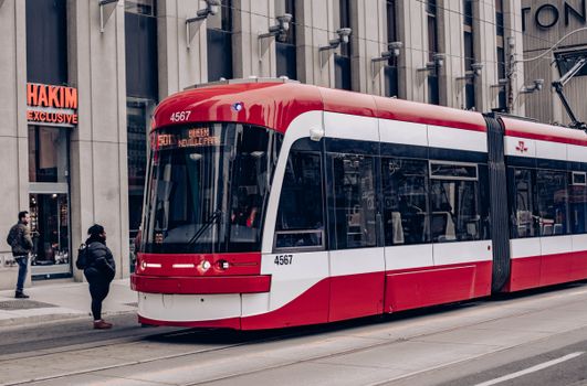 Red streetcar on city street with passengers and buildings in background.