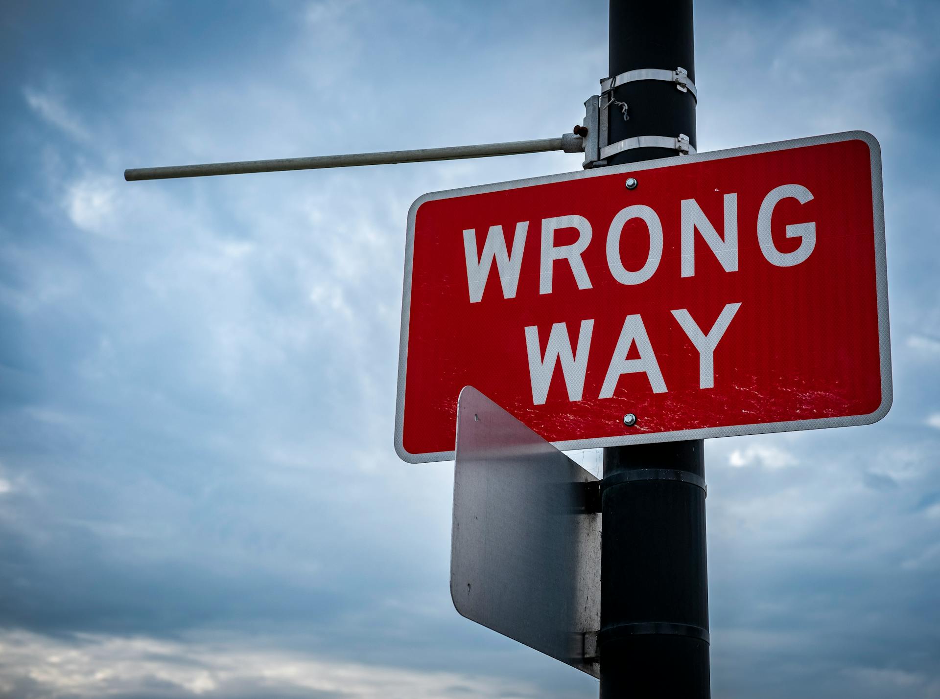 A close-up of a red wrong way road sign against an overcast sky, symbolizing caution.