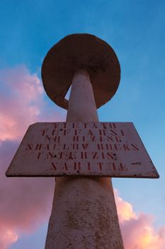 Rustic metal pole with warning sign against dramatic sunset sky with pink clouds.