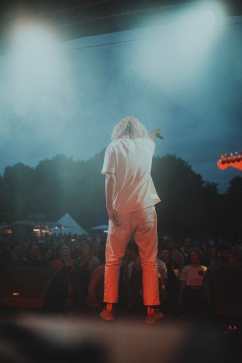 Free Back view of a performer on stage with an enthusiastic audience at an outdoor concert. Stock Photo