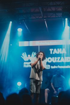 Musician passionately singing at a vibrant indoor concert with dramatic lighting.