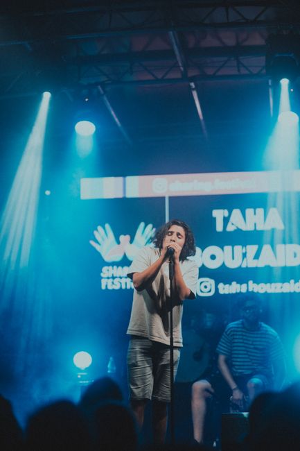 Musician passionately singing at a vibrant indoor concert with dramatic lighting.