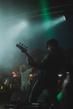 Energetic performance by a guitarist at an outdoor concert under dramatic lighting.