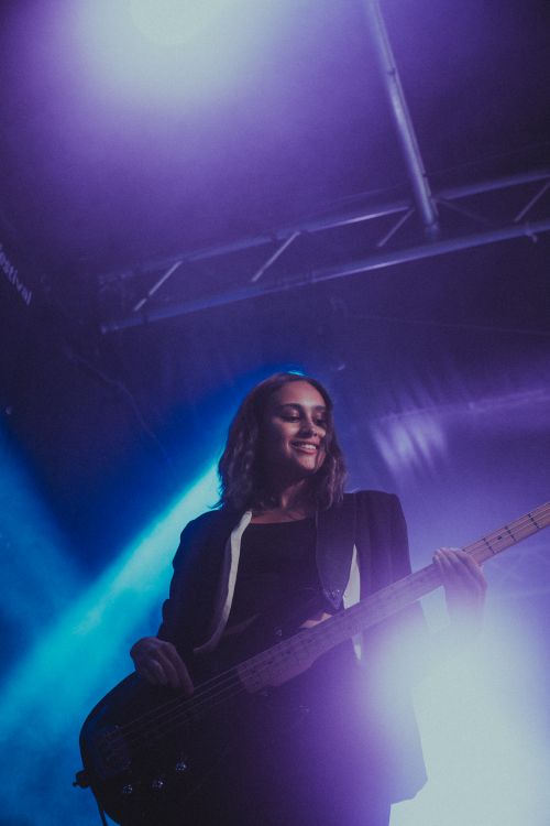 Free Woman playing bass guitar on stage with moody, vibrant lighting during a live performance. Stock Photo