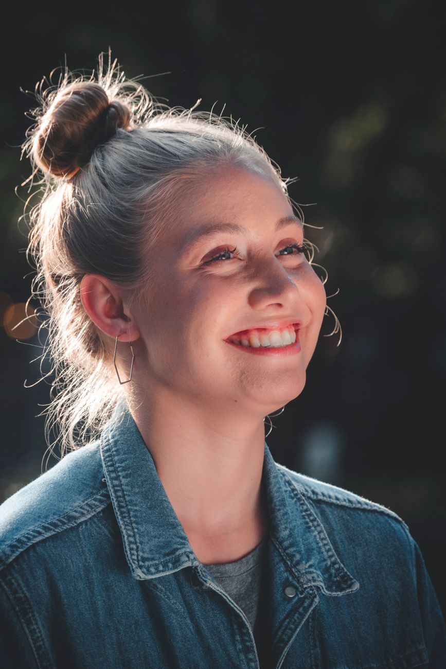 Portrait of a smiling woman in a denim jacket with natural lighting.