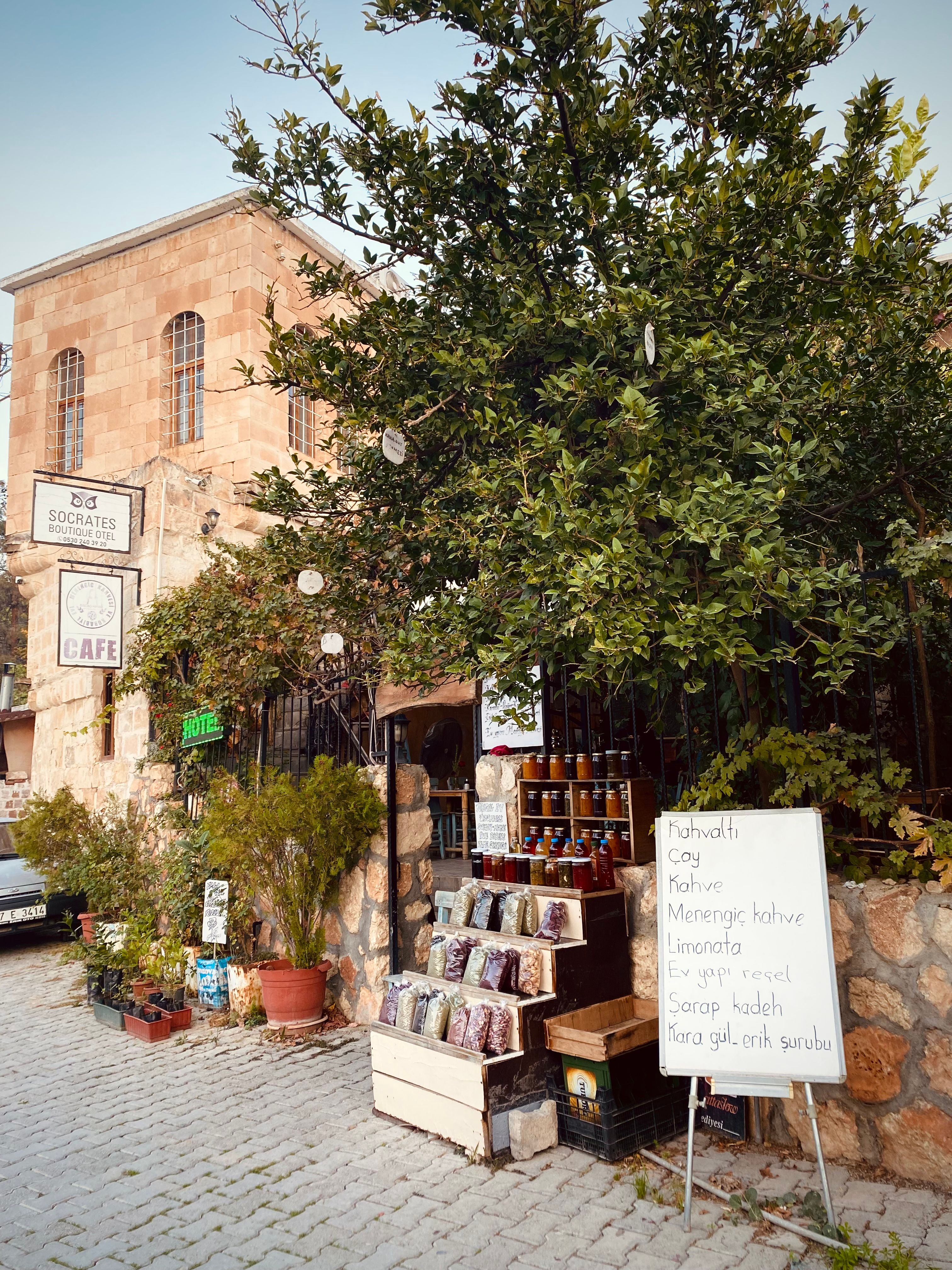 Street view of a cafe and local market in Halfeti, Turkey with vibrant greenery.