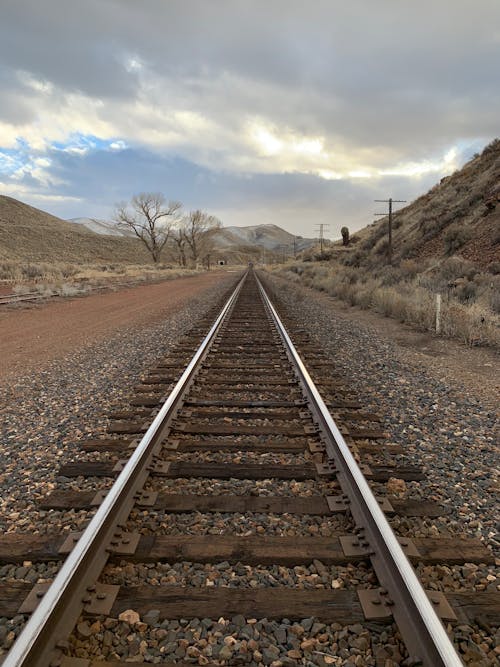 An Empty Railway Between Brown Field Under Cloudy Sky