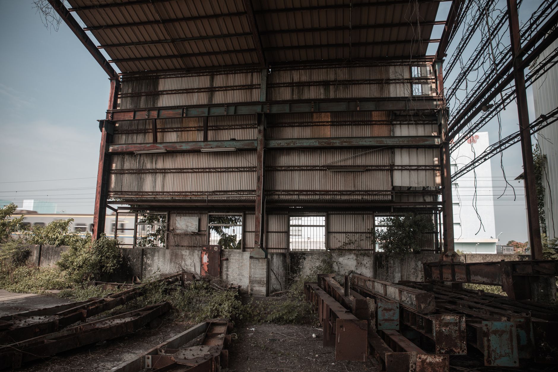 An abandoned industrial site with rusty beams and overgrown vegetation, showcasing decay.