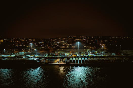Aerial view of an urban port with colorful cargo containers at night, along a waterfront.