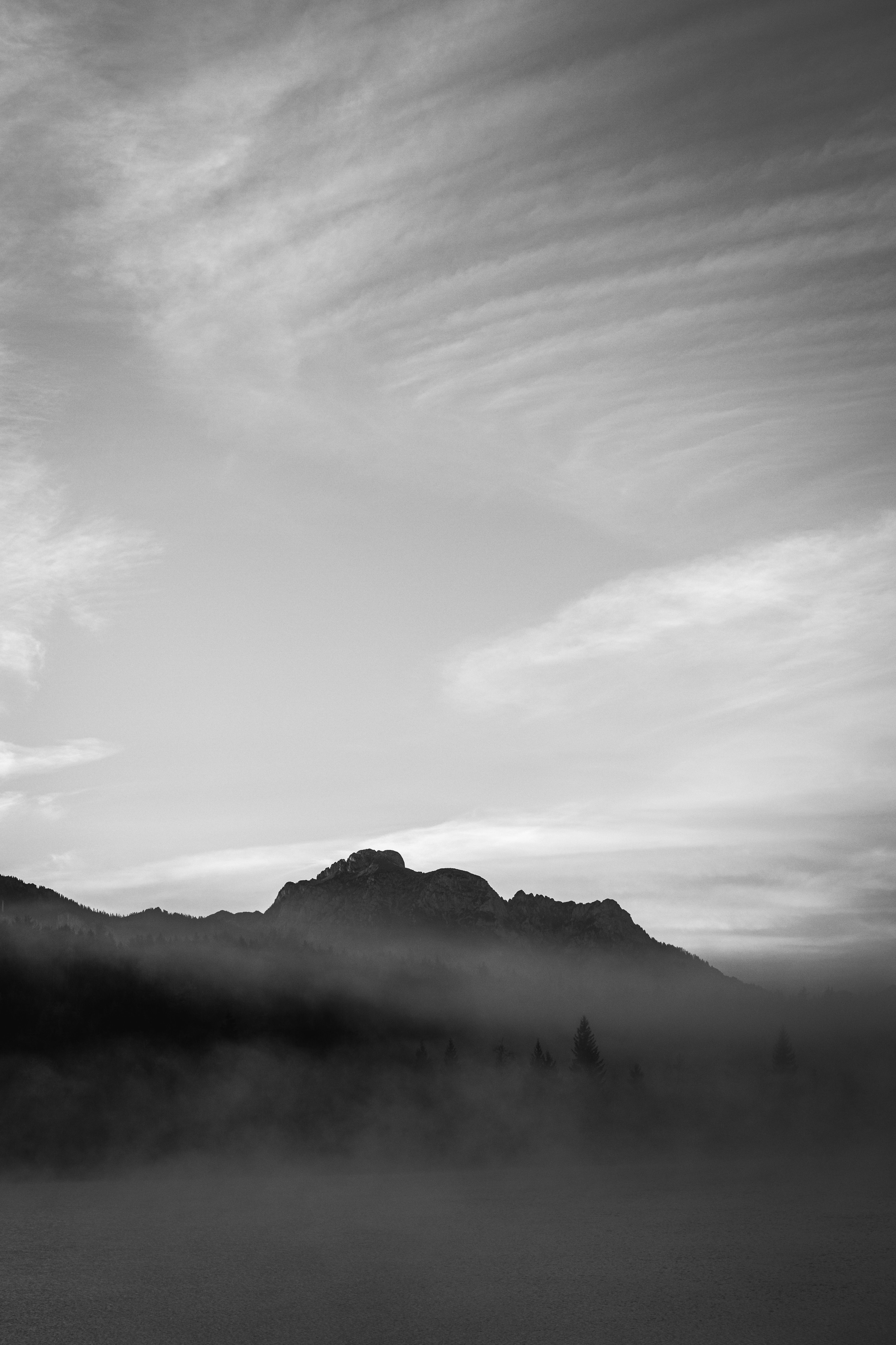 Serene black and white shot of a foggy mountain at dawn with dramatic clouds.