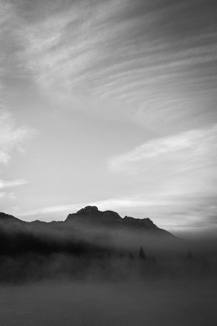 Serene black and white shot of a foggy mountain at dawn with dramatic clouds.