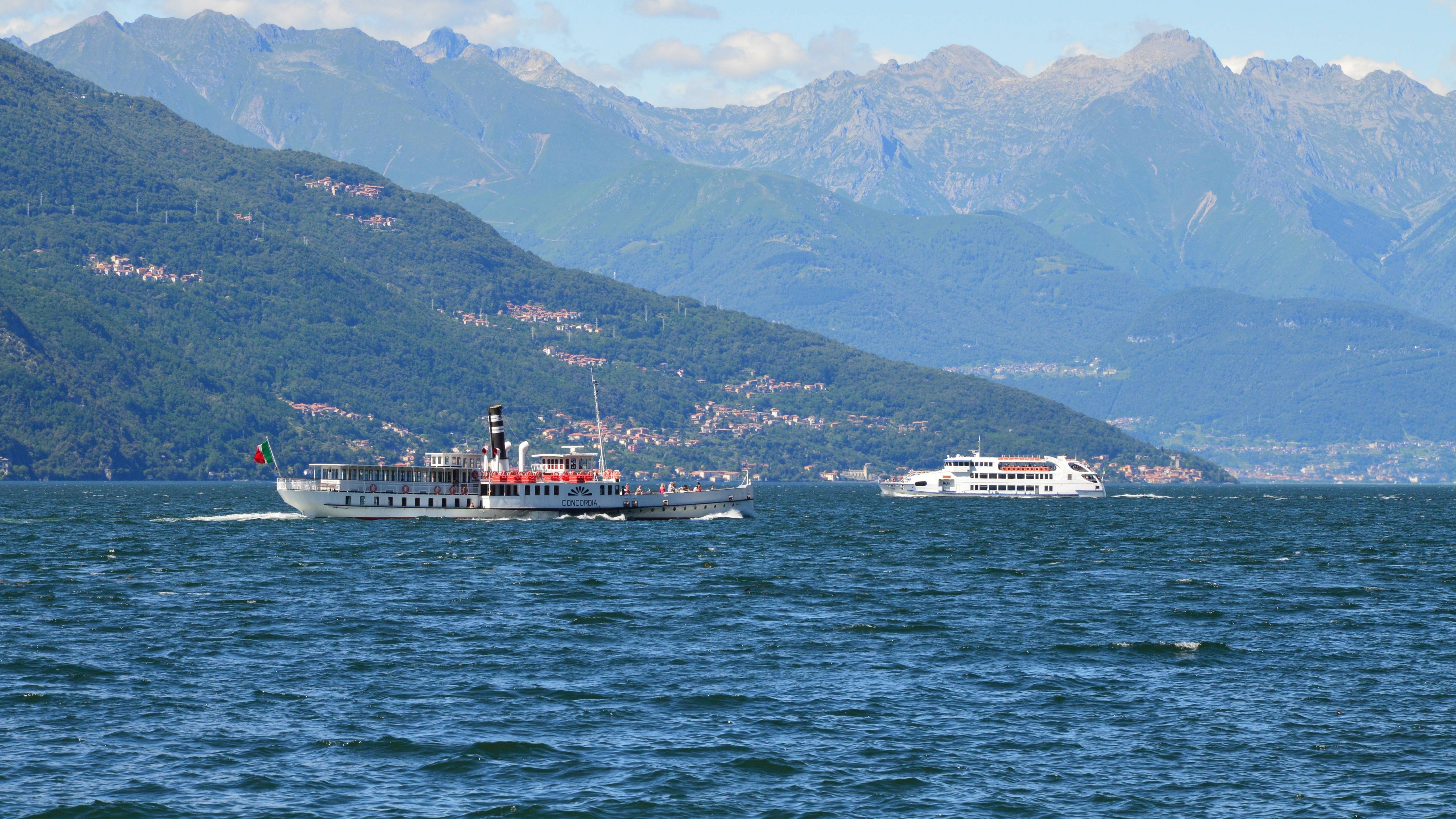 Two boats cruise across Lake Como with mountainous backdrop under clear blue skies.