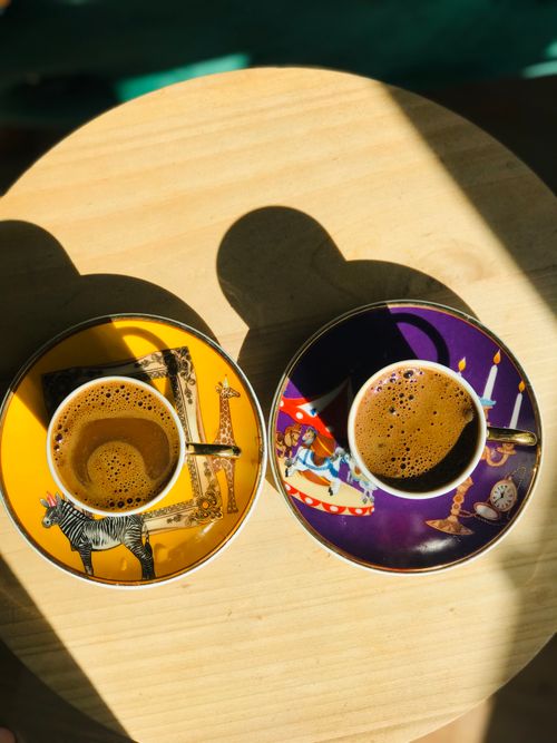 Free Two cups of coffee with artistic animal saucers on a sunlit wooden table. Stock Photo