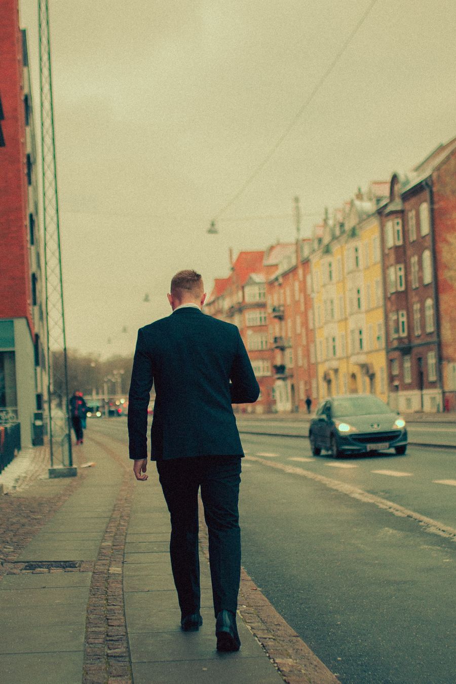 Back view of a well-dressed man walking a European street at dusk — anonymous sample stock photo (NOT a photo of you), replace with your own portrait
