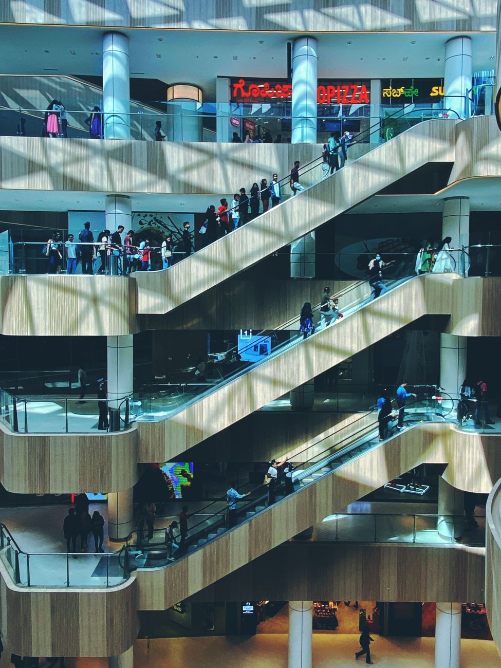 Crowded shopping mall with multiple escalators in Bengaluru, India.