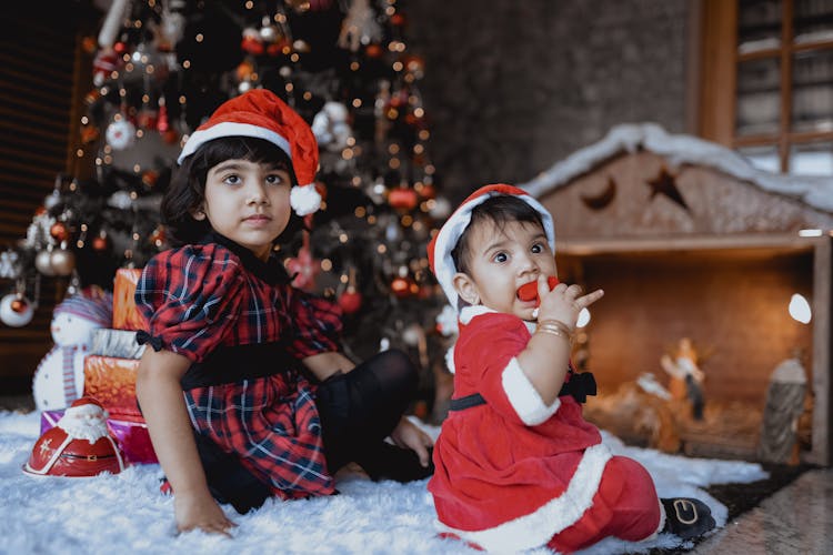 A Girl And A Baby On Carpet Near A Christmas Tree