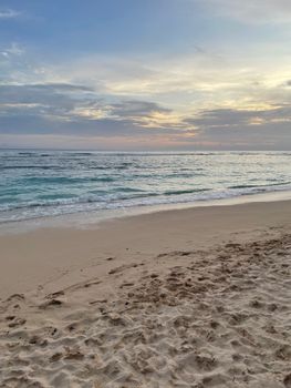 Calm beach scene at sunrise, gentle waves lapping on sandy shore under cloudy sky.
