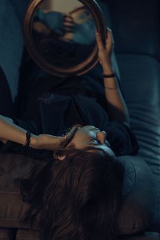 Moody artistic portrait of a woman lying indoors with mirror reflection.