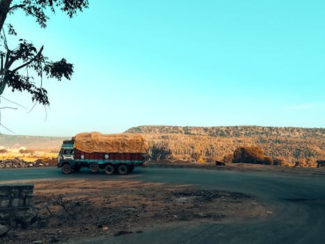 A truck travels on a rural road with scenic hillside view under a bright sky.