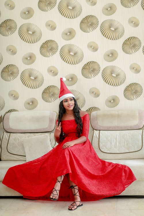 Free A young woman in a red dress and Santa hat posing indoors on a sofa, exuding holiday cheer. Stock Photo