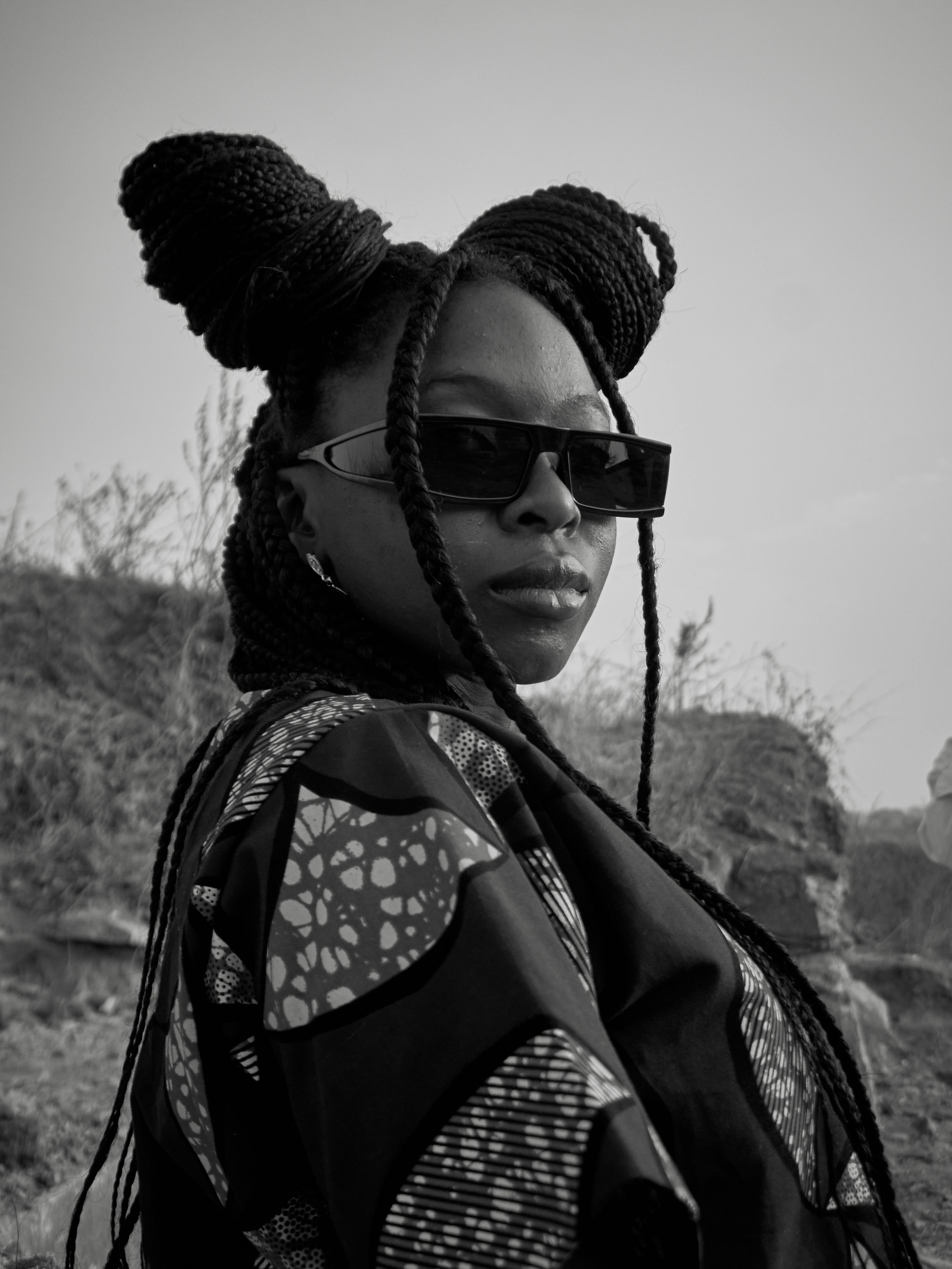 Black woman confidently posing with braids and sunglasses outdoors.
